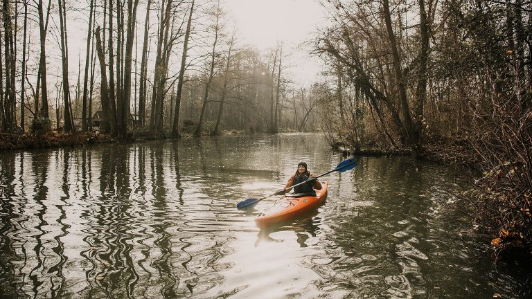 Kanutour im Spreewald im Winter Person in einem Kanu vor winterlicher Landschaft und kahlen Bäumen
